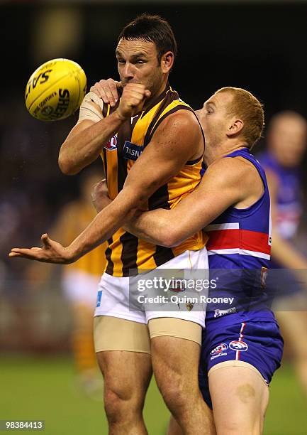 Brent Guerra of the Hawks handballs whilst being tackled by Adam Cooney of the Bulldogs during the round three AFL match between the Western Bulldogs...