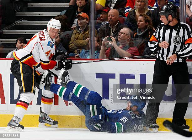 Henrik Sedin of the Vancouver Canucks is checked to the ice by Jay Bouwmeester of the Calgary Flames as referee Brad Meier looks on during their game...