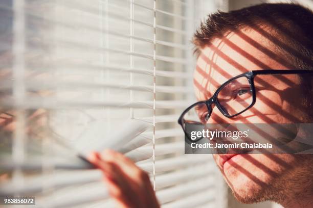 curious man looking through a jalousie - jalousie stockfoto's en -beelden