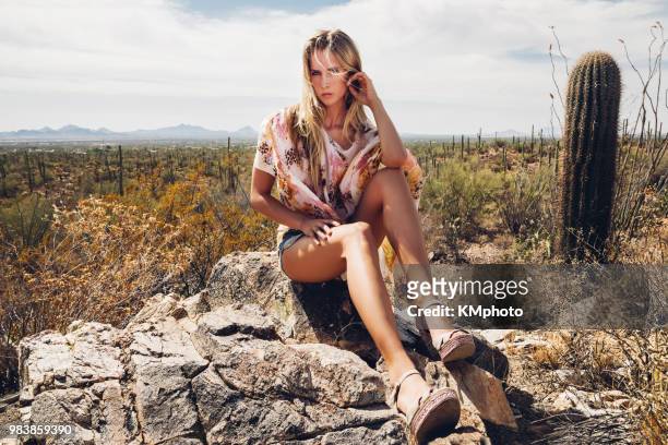 blonde girl sitting on stone with cactus kmphoto - kmphoto stock pictures, royalty-free photos & images