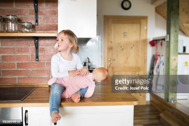 little girl with doll sitting on kitchen countertop - doll house stockfoto's en -beelden