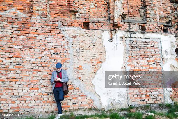senior man with smartphone against brick wall, texting. - bumthang fotografías e imágenes de stock