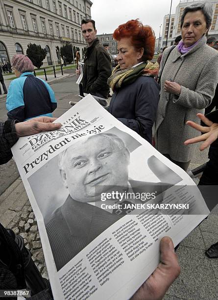 People collect free copies of a newspaper with the front page carrying a photograph of late president Lech Kaczynski, outside the presidential palace...