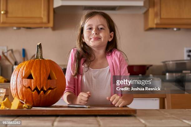 proud little girl standing beside jack-o-lantern pumpkin in kitchen - jack o lantern bildbanksfoton och bilder