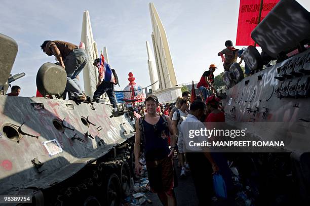 Western tourist walks past "Red Shirt" protesters standing on top an abandoned Thai army armoured after overnight clashes in central Bangkok on April...