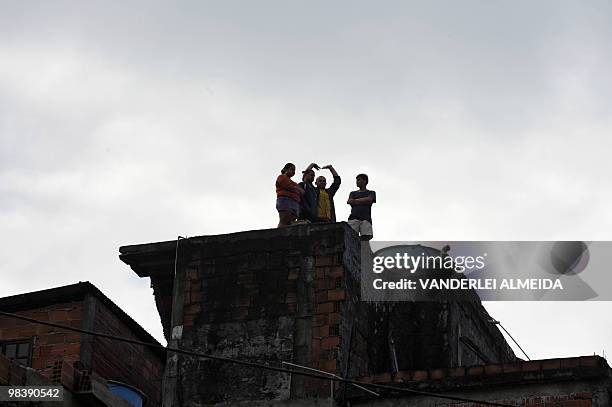 People on a rooftop observe workers below with heavy machinery digging in the mud left by a landslide at Vicoso Jardim Bumba shantytown in Niteroi,...