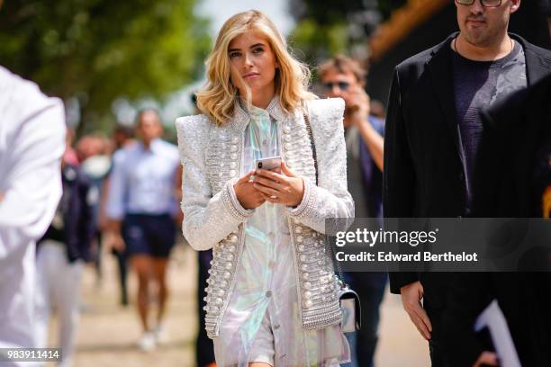 Xenia Adonts wears a white gliter tweed jacket with pearls, a white shiny dress, outside Balmain, during Paris Fashion Week - Menswear Spring-Summer...