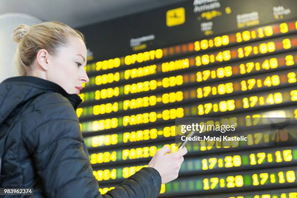 woman at airport in front of flight information board checking her phone. - departure board front on stockfoto's en -beelden
