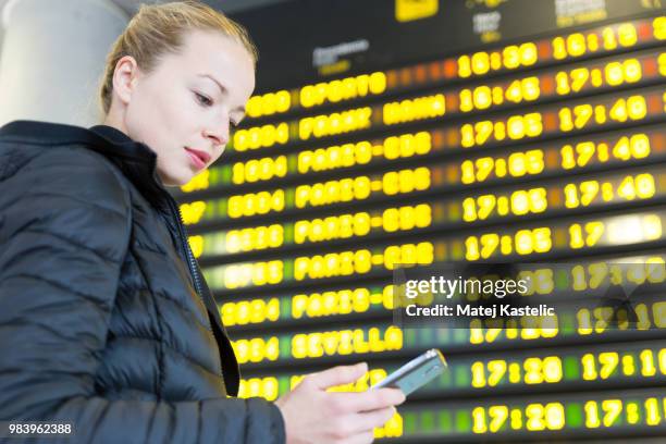 woman at airport in front of flight information board checking her phone. - departure board front on stockfoto's en -beelden