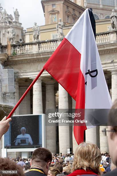 Faithful hold Polish flag at St. Peter's Square as Pope Benedict XVI displayed on a Tv screen delivers his Regina Coeli Prayer from his summer...