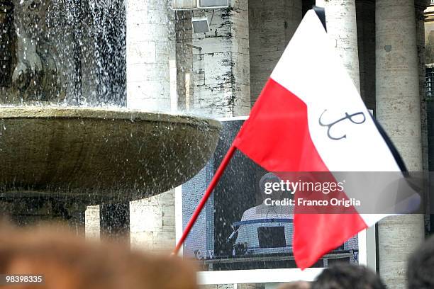 Faithful holds a Polish flag at St. Peter's Square as Pope Benedict XVI displayed on a TV screen delivers his Regina Coeli Prayer from his summer...