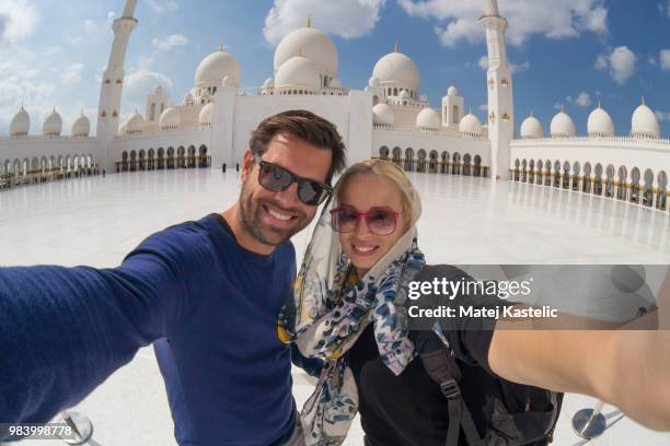 couple taking selfie in sheikh zayed grand mosque, abu dhabi, united arab emirates. - moskee toerisme stockfoto's en -beelden