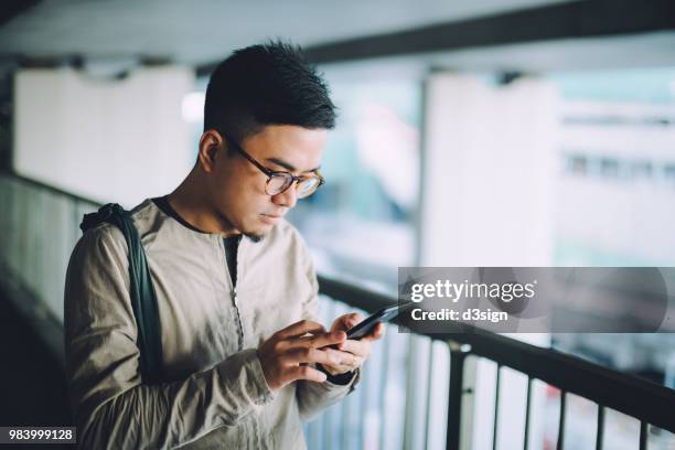 smart young man text messaging on mobile phone on the way to work on urban bridge in city in the morning - mobile banking stockfoto's en -beelden