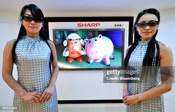 Models wearing 3-D glasses pose next to Sharp Corp.'s four-primary-color 3-D liquid-crystal display panels at a media preview in Tokyo, Japan, on...