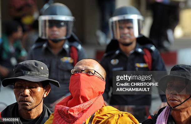 Buddhist monk wearing a red scarf around his mouth stands beside anti-government guards and riot police at the Police General Hospital near the site...