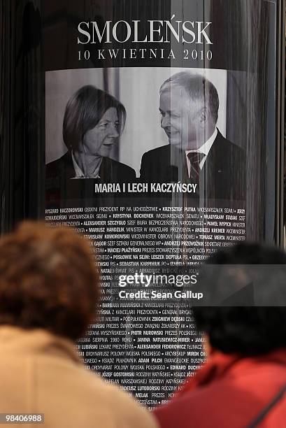 People stop to look at a poster showing late Polish President Lech Kaczynski and his wife Maria, as well as a list of all the other people who were...