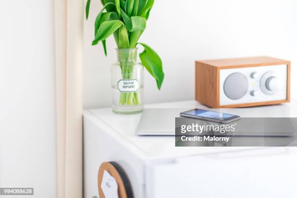 radio, rolled world map and glass vase with tulips, laptop and smartphone standing on refrigerator in the kitchen. plus shopping list. - radio stockfoto's en -beelden