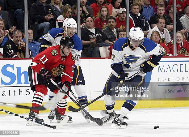 John Madden of the Chicago Blackhawks and David Perron of the St. Louis Blues skate toward the puck as Andy McDonald of the Blues watches from...