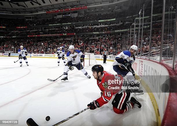 Andrew Ladd of the Chicago Blackhawks reaches toward the puck as Eric Johnson and Jay McClement of the St. Louis Blues watch from behind during the...
