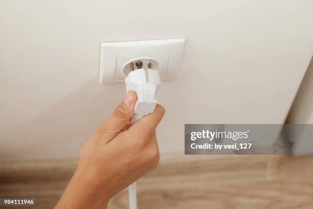 hand plugging in or out an electric cord into a socket - plugging in stockfoto's en -beelden