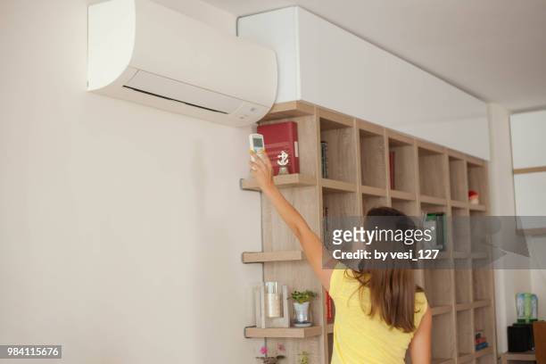 girl turning on wall mounted air-conditioner at home - air conditioner - fotografias e filmes do acervo