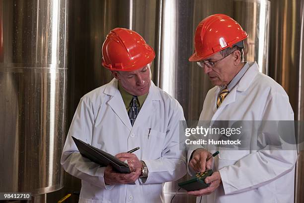 two scientists with monitoring and record keeping equipment in a chemical plant - clipboard and glasses imagens e fotografias de stock