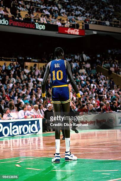 Manute Bol of the Golden State Warriors stands on the court against the Boston Celtics during a game played in 1989 at the Boston Garden in Boston,...