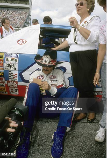 Nascar driver Richard Petty in this portrait sitting next to the STP car signing an autograph for a fan February 18, 1990 before the Nascar Winston...