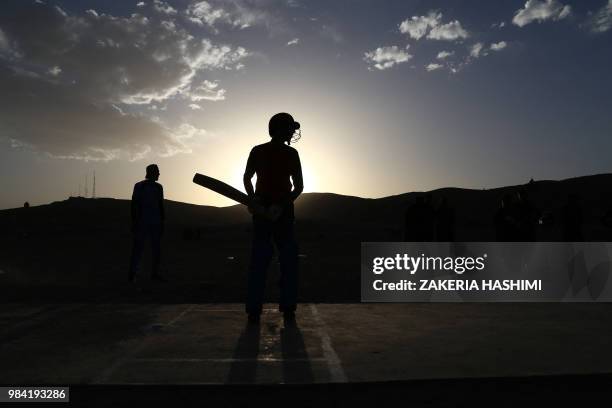 In this photograph taken on June 25, 2018 Afghan youths play cricket in a field as the sun sets in Ghazni province.