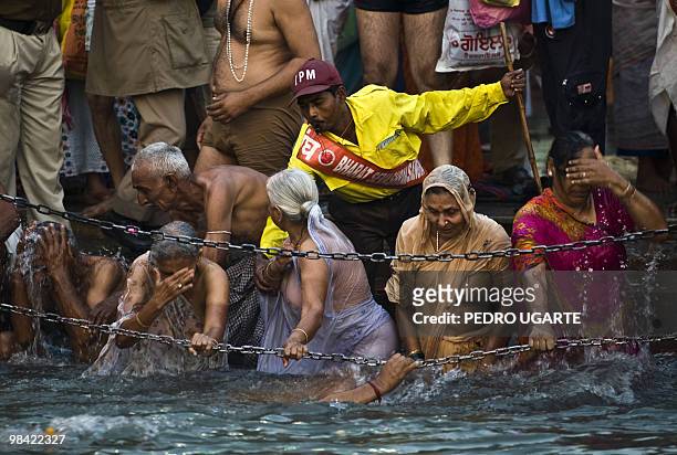 Man helps Hindus as they bathe in the river Ganges during the Kumbh Mela festival in Haridwar on April 13, 2010. The world's largest religious...