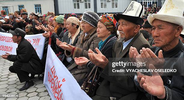 Supporters of ousted Kyrgyz President Kurmanbek Bakiyev pray as they stand behind a poster reading "Bloody Government!" during a rally in Jalal-Abad...