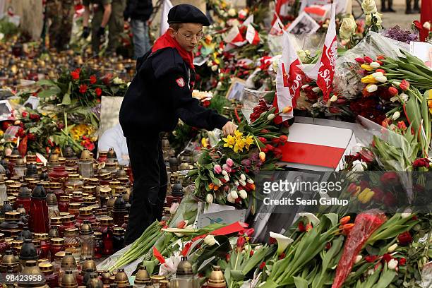 Polish boy scout arranges flowers left by mourners next to a portrait of late Polish President Lech Kaczynski and his wife Maria Kaczynska outside...
