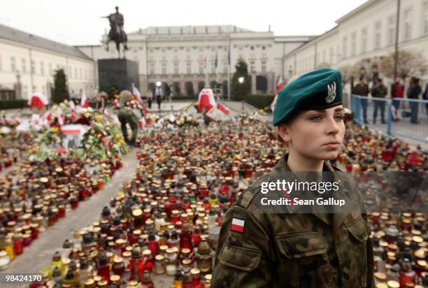 Female Polish soldier stands among candles and flowers left by mourners outside the Presidential Palace in memory of late Polish President Lech...