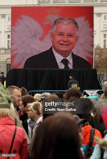 Mourners stand in front of a large screen television monitor presenting a slide show of late Polish President Lech Kaczynski outside the Presidential...