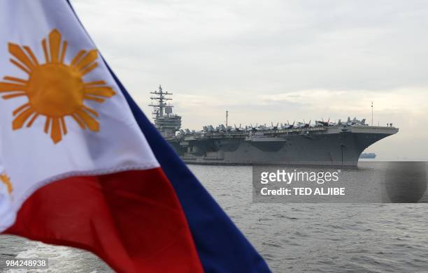 Philippine flag flutters as the nuclear-powered aircraft carrier USS Ronald Reagan is seen anchored off Manila bay on June 26, 2018. - A US aircraft...
