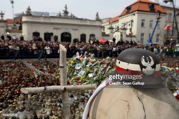 World War II-era helmet and a wooden cross stand among mourners and flowers outside the Presidential Palace following the arrival of the coffin of...
