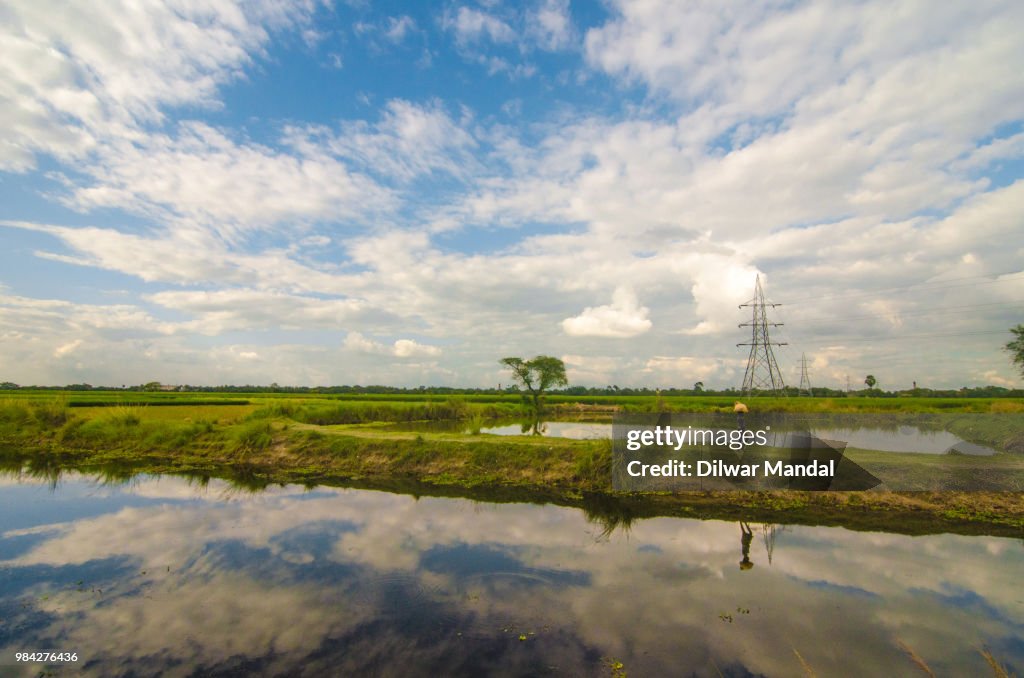 A farmer is walking behind a small lake in a village