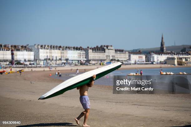 Man carries a paddle board down to the sea as people enjoy the fine weather as they spend the day on the beach at Weymouth seafront on June 26, 2018...