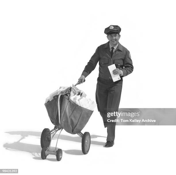 Full-length portrait of a smiling mailman as he pushes a mail carrier with one hand and holds several letter in the other, 1967.