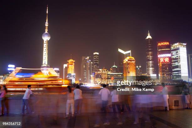 Tourists on the Bund at sunset look out over the cityscape and skyline of Pudong Financial District over Huang Pu River in Shanghai, China. Every day...