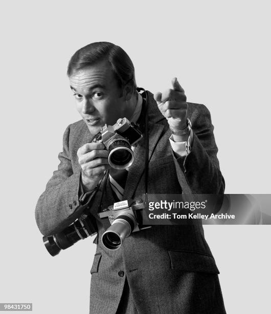 View of a photographer, with three cameras around his neck, as he holds one up and points a finger, 1970.