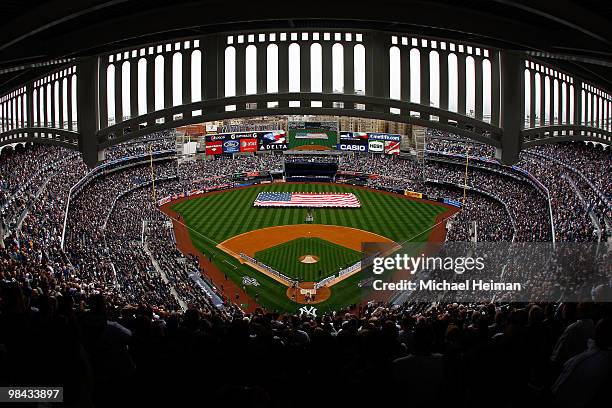 The New York Yankees and the Los Angeles Angels of Anaheim stand at attention during the National Anthem as a giant American flag is displayed on the...