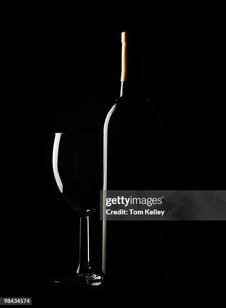 View of an empty wine glass and an uncorked bottle, seen illuminated from the side, against a black background, 2009.