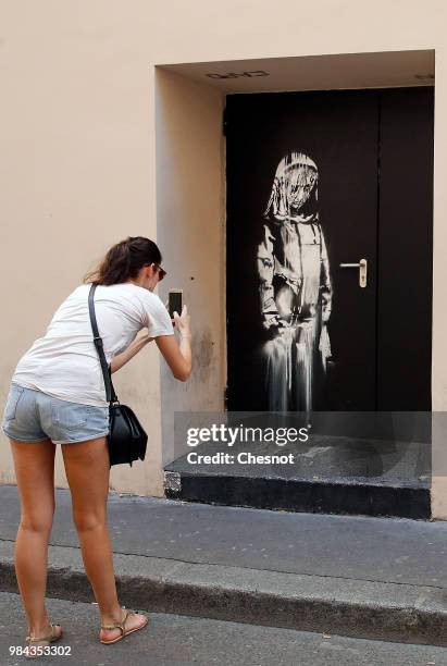 Woman takes a picture of a recent artwork attributed to street artist Banksy on June 26, 2018 in Paris, France. Yesterday a new artwork attributed to...