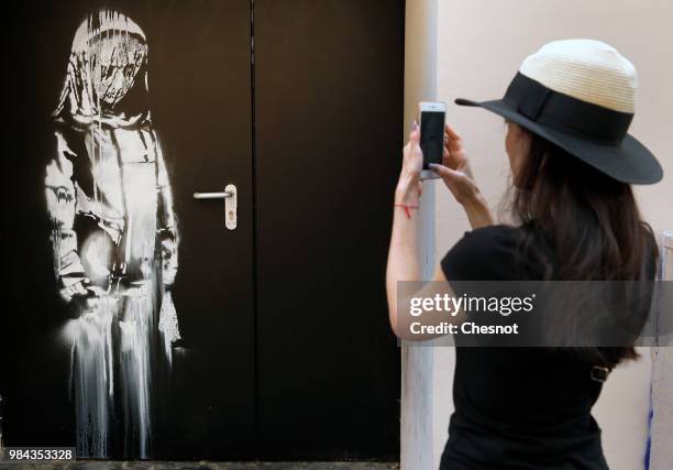 Woman takes a picture of a recent artwork attributed to street artist Banksy on June 26, 2018 in Paris, France. Yesterday a new artwork attributed to...