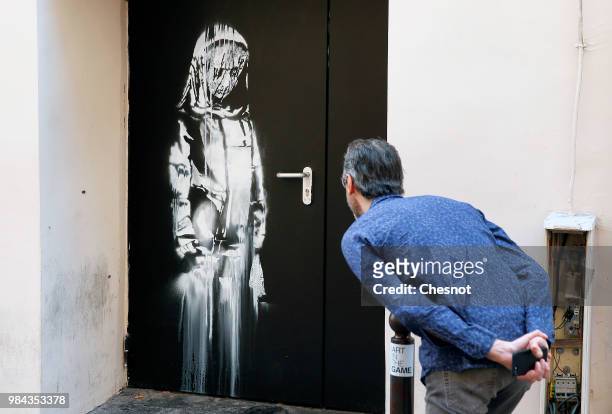 Man views a recent artwork attributed to street artist Banksy on June 26, 2018 in Paris, France. Yesterday a new artwork attributed to street artist...