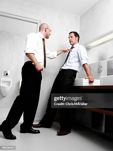 two businessmen having argument in public restroom - office bathroom stock-fotos und bilder