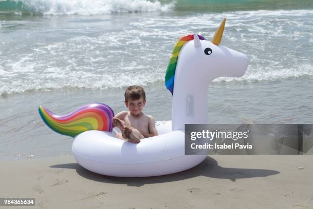 little boy lying on inflatable unicorn at beach - isabel pavia stock-fotos und bilder