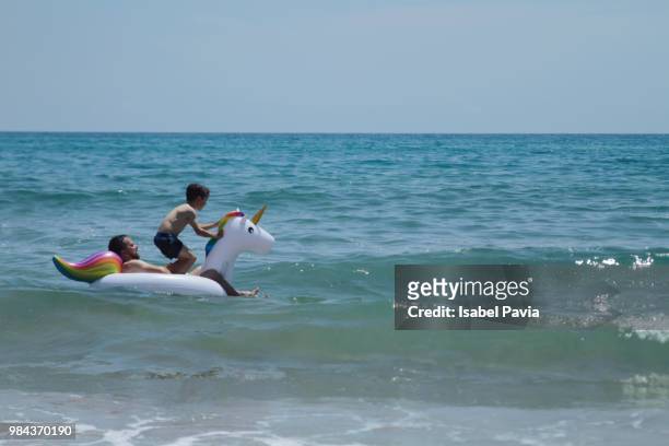 father and son playing on inflatable unicorn at sea - isabel pavia stockfoto's en -beelden
