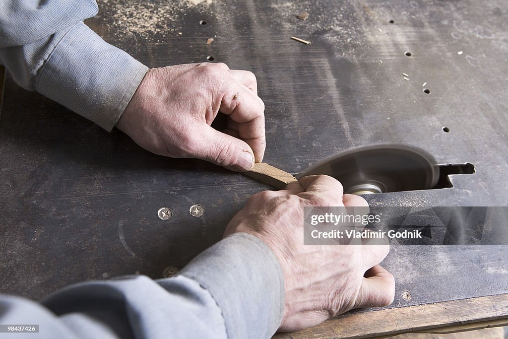 Close-up of carpenter cutting piece of wood with buzz saw